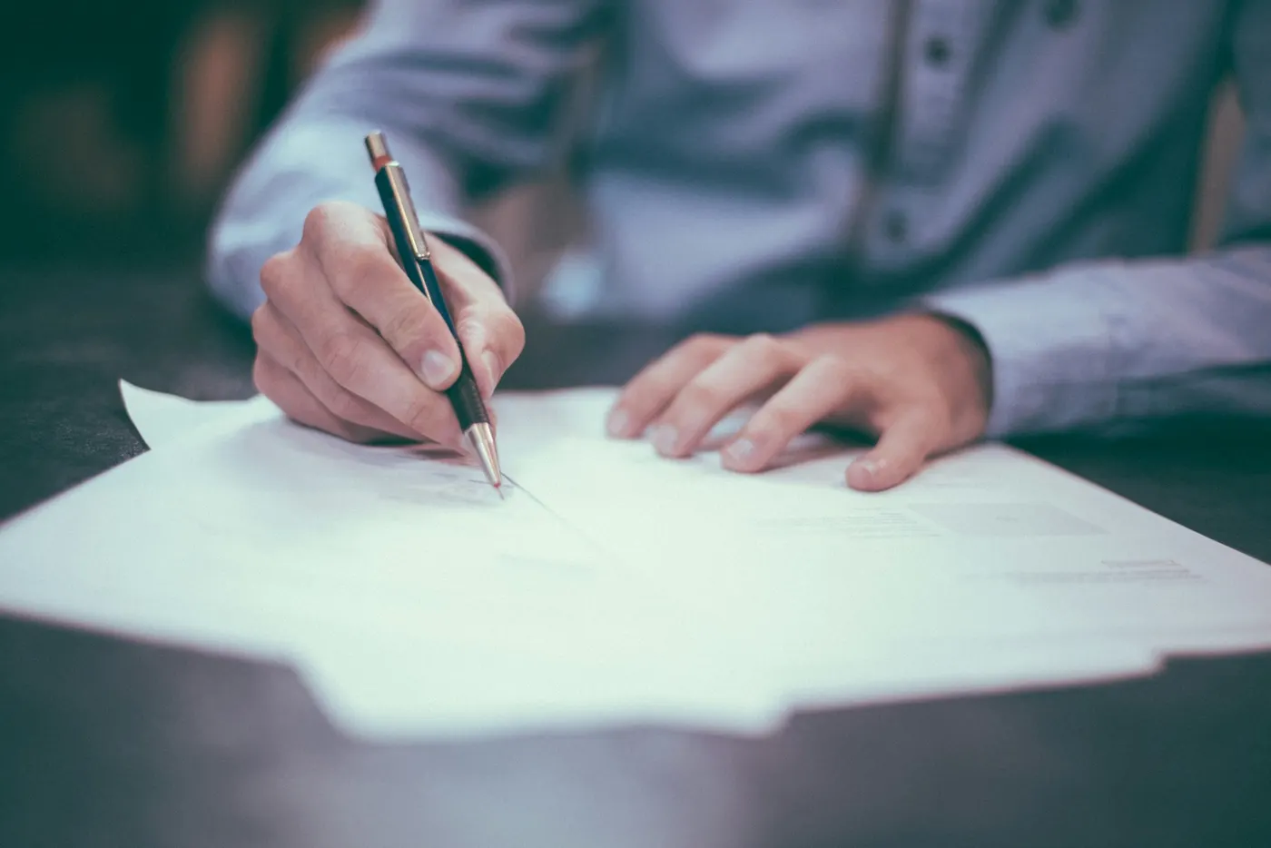 A person signing business documents at a desk